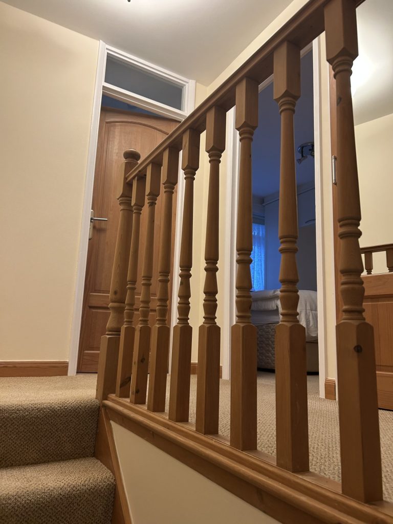 Wooden stair balustrade with beige carpeted steps and painted hallway walls.