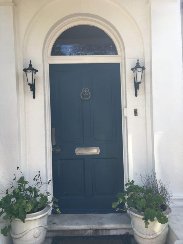 Blue front door with arched surround and black wall lanterns on a white exterior.
