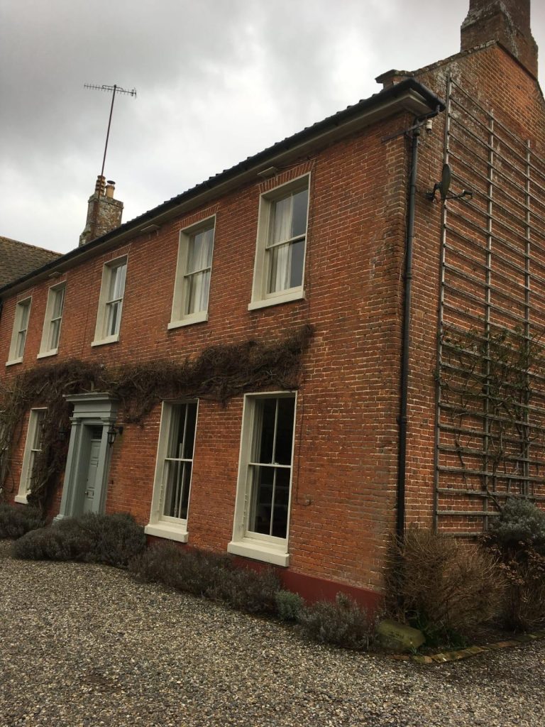 Red brick house exterior with cream window frames and a gravel driveway.