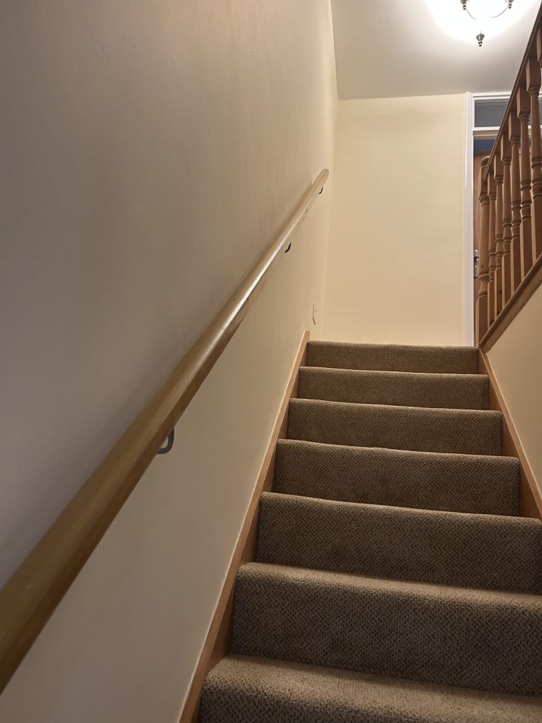 Carpeted staircase with wooden handrail and beige painted walls leading to an upper landing.
