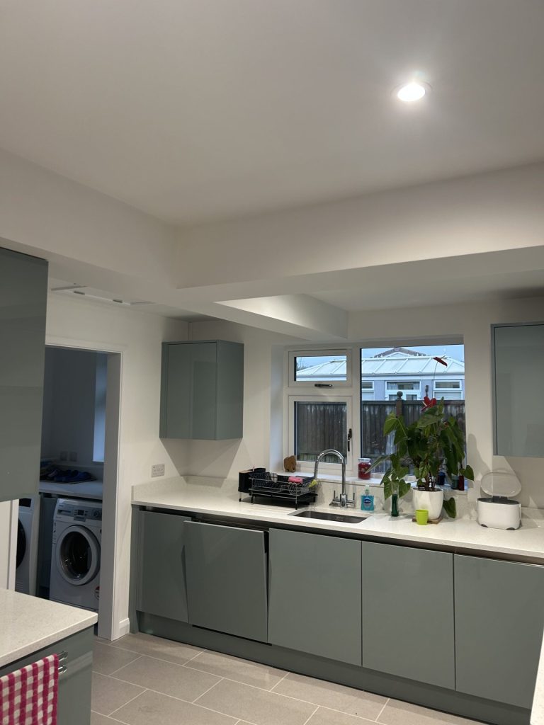 Modern kitchen with sage green cabinets, white worktops and recessed ceiling lighting.