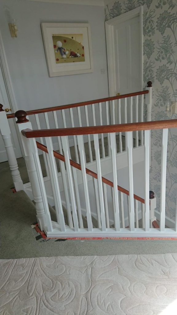 White painted stair balustrade with wooden handrail and patterned wallpaper.